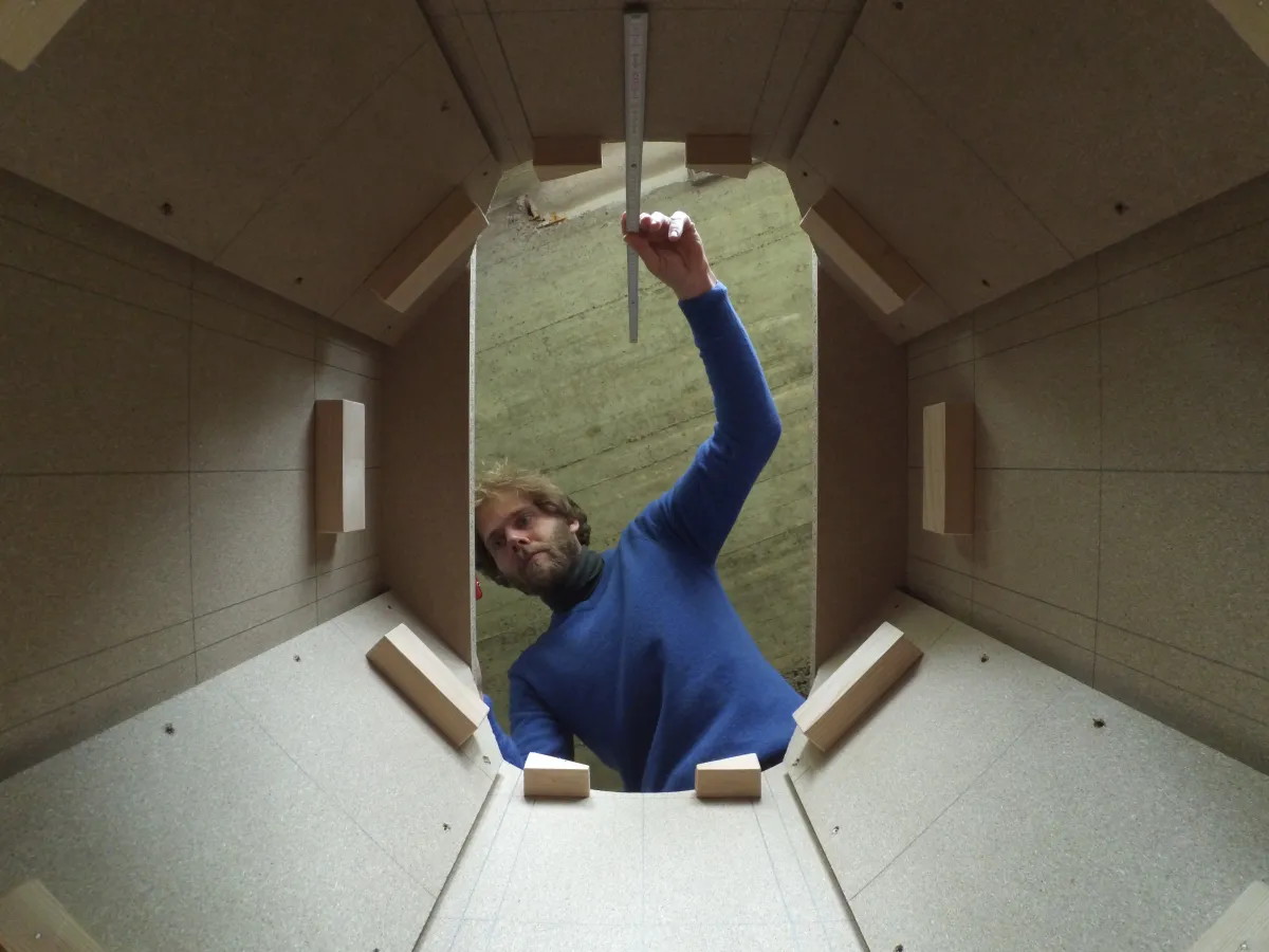 Jan Wolf misst in der Werkstatt mit dem Zollstock in einem Gehäuse aus Holzplatten